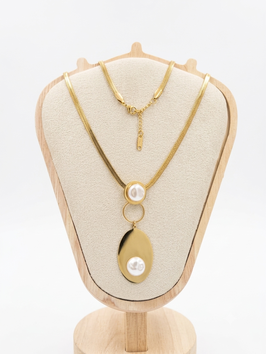 Gold chain necklace with a double-ring pendant featuring a large oval gold disc and a small white pearl, displayed on a beige jewelry bust.