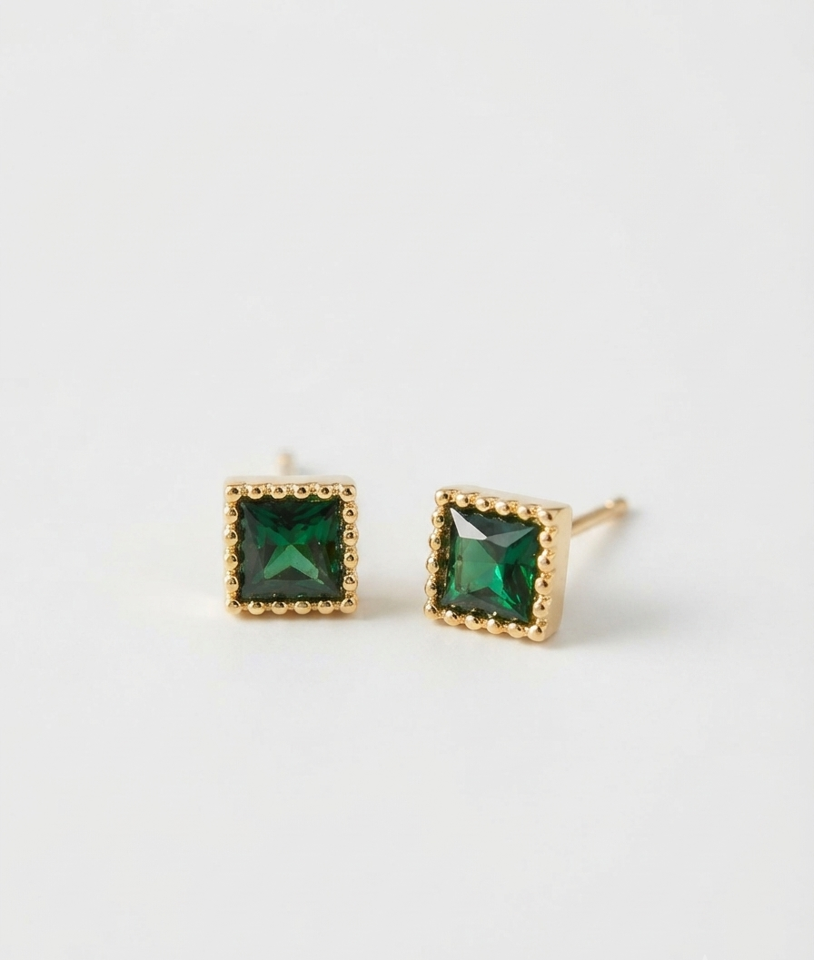 A pair of gold stud earrings with square-cut green gemstones, set in a beaded gold border and shown on a clean white background.