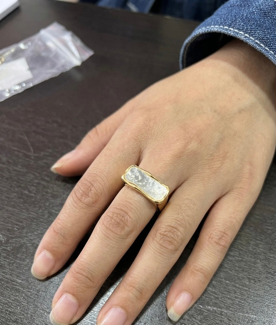 Gold horizontal bar ring with white iridescent inlay worn on hand.