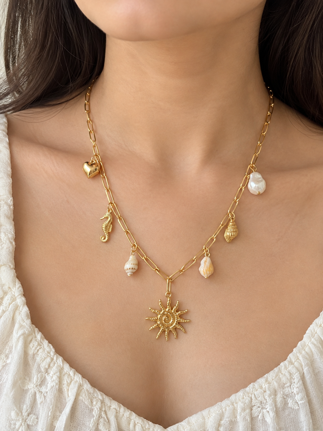 A close-up of a model wearing a gold double-strand necklace with seashell and seahorse charms, featuring a central sun pendant.