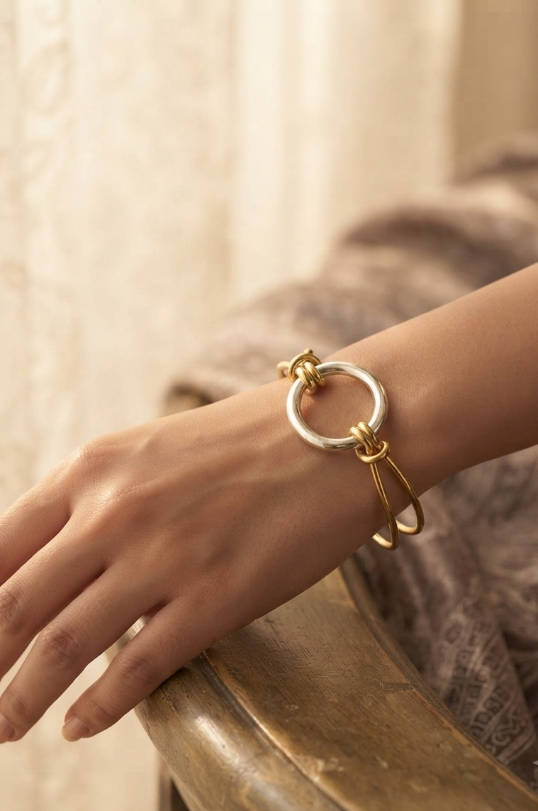 Gold and silver two-tone open kada bracelet with interlocking twisted knot design on a cream background