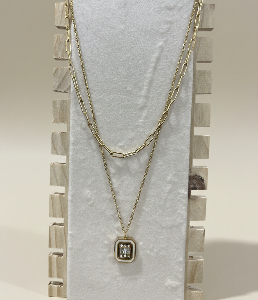 A tarnish resistant double strand necklace in gold finish with a geometric pendant displayed on a professional wooden stand