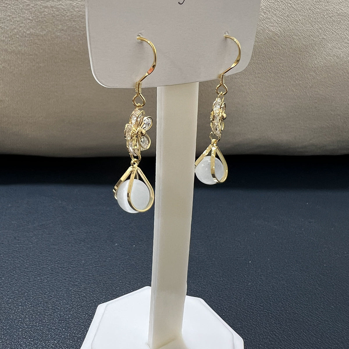 Pair of stainless steel flower drop earrings displayed on a white jewelry stand showing the elegant dangle style