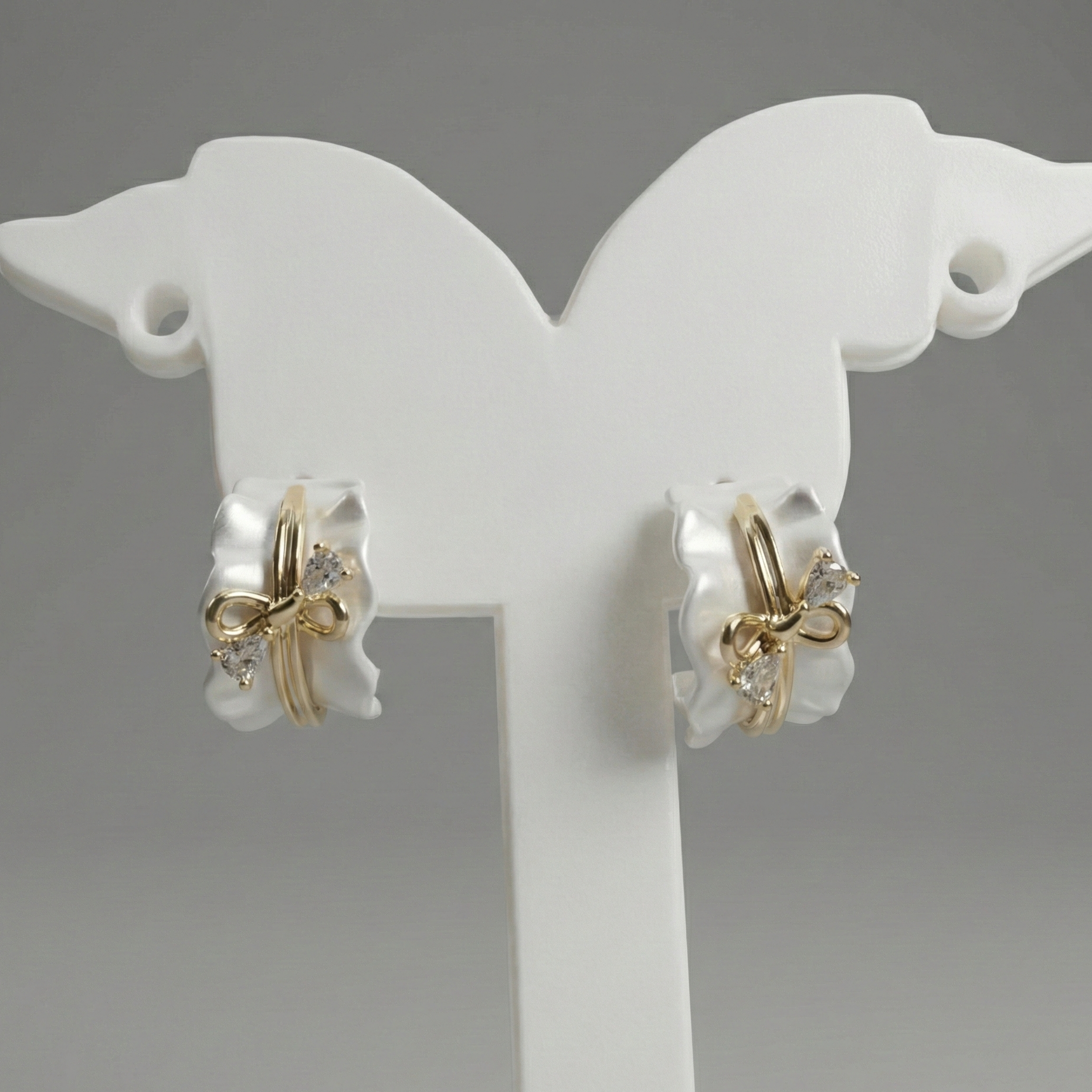 Pair of gold and silver earrings on a white stand against a gray background