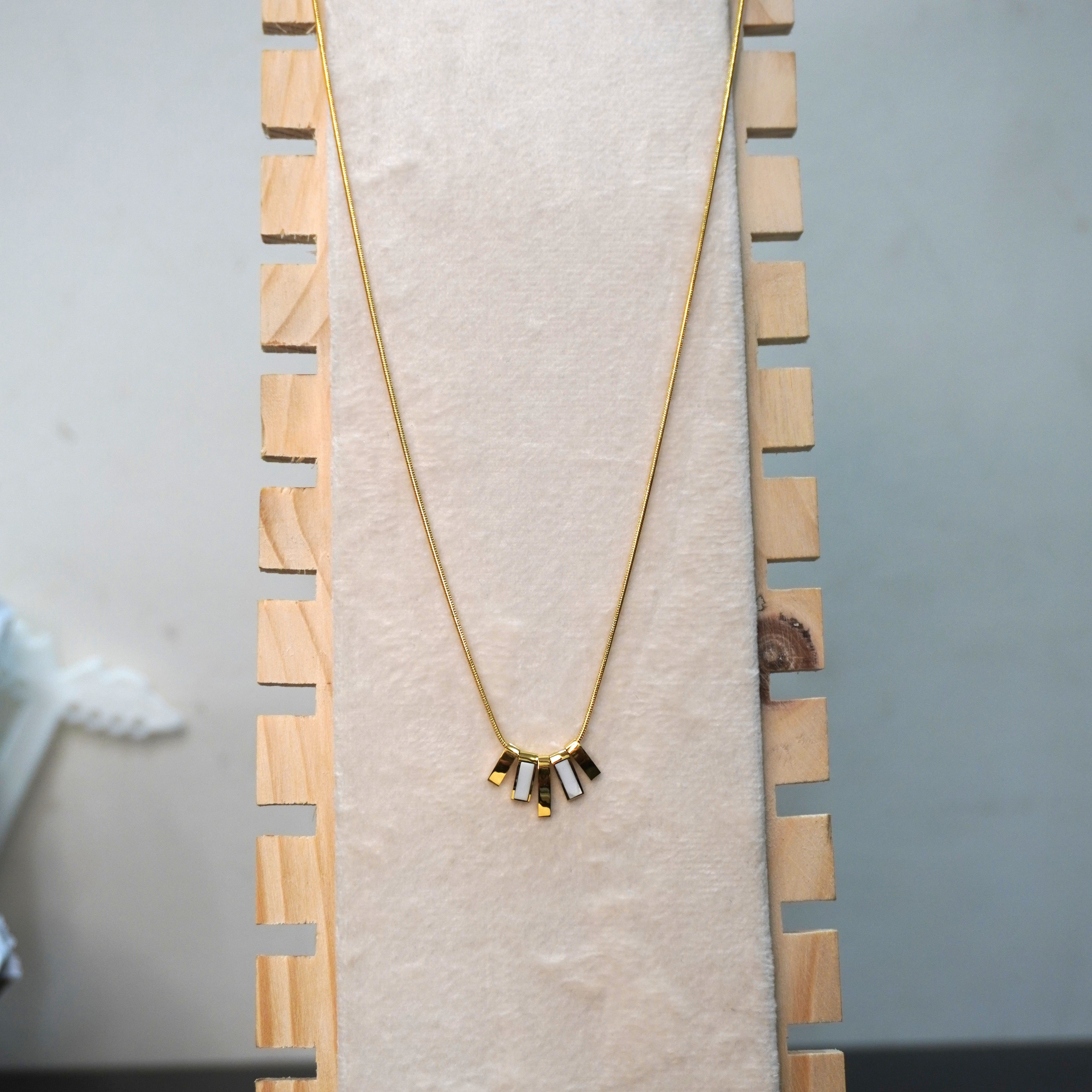 Gold necklace with a geometric pendant on a wooden stand against a neutral background