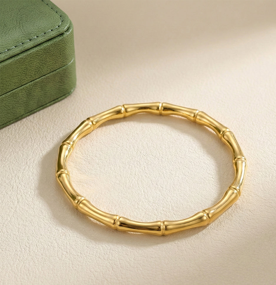 Top down view of a gold plated bamboo motif bangle resting on a textured neutral surface