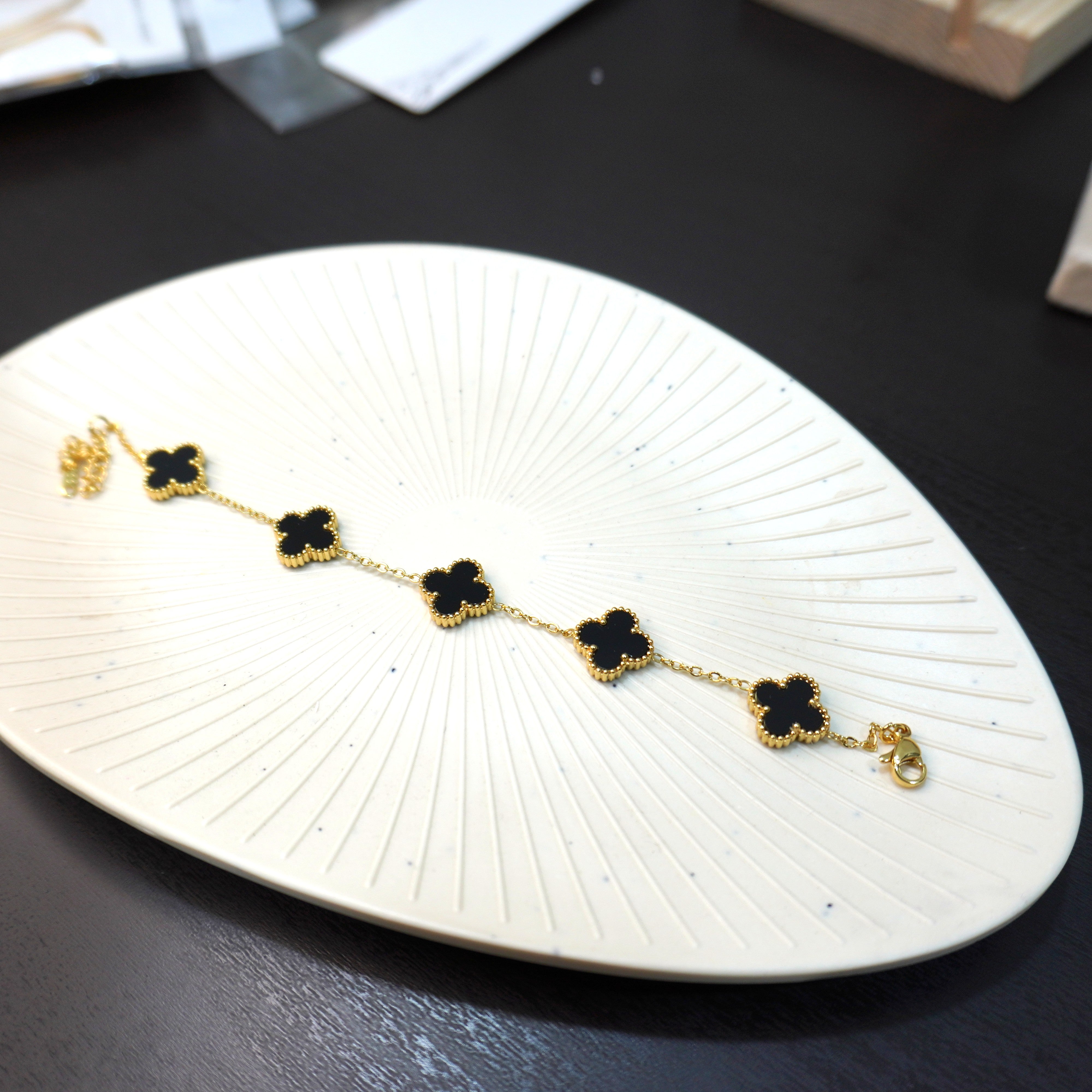 Gold and black floral bracelet on a white dish with blurred background