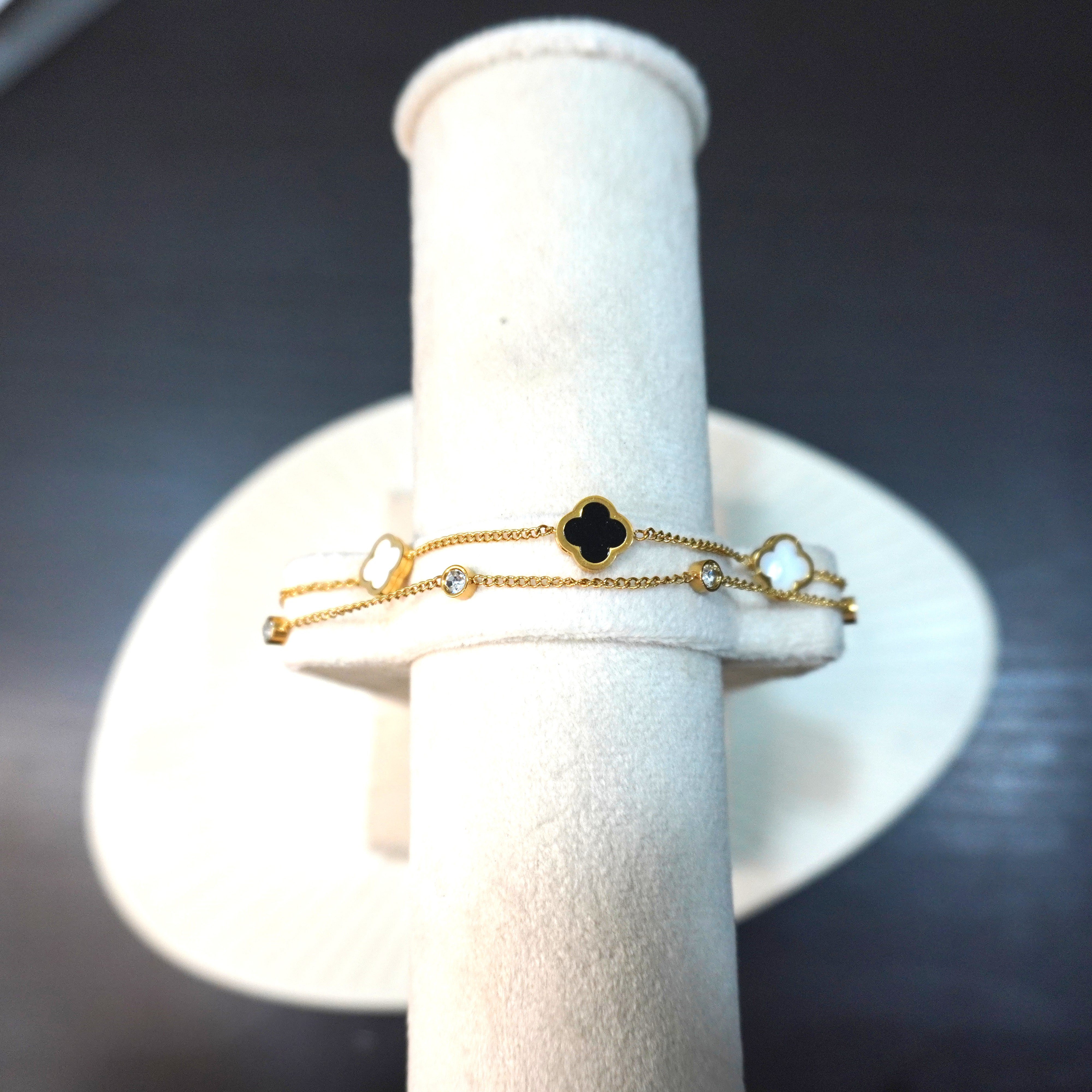 Gold bracelet with clover design on a white stand against a dark background