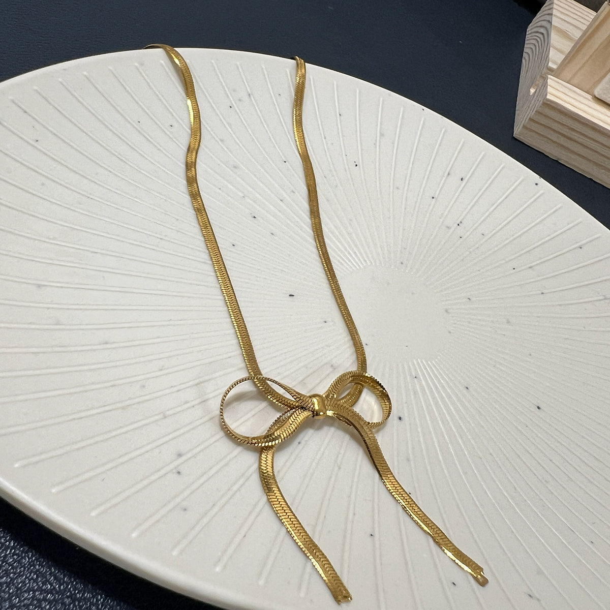 Premium anti-tarnish bow necklace in gold-toned stainless steel draped over a wooden jewelry stand