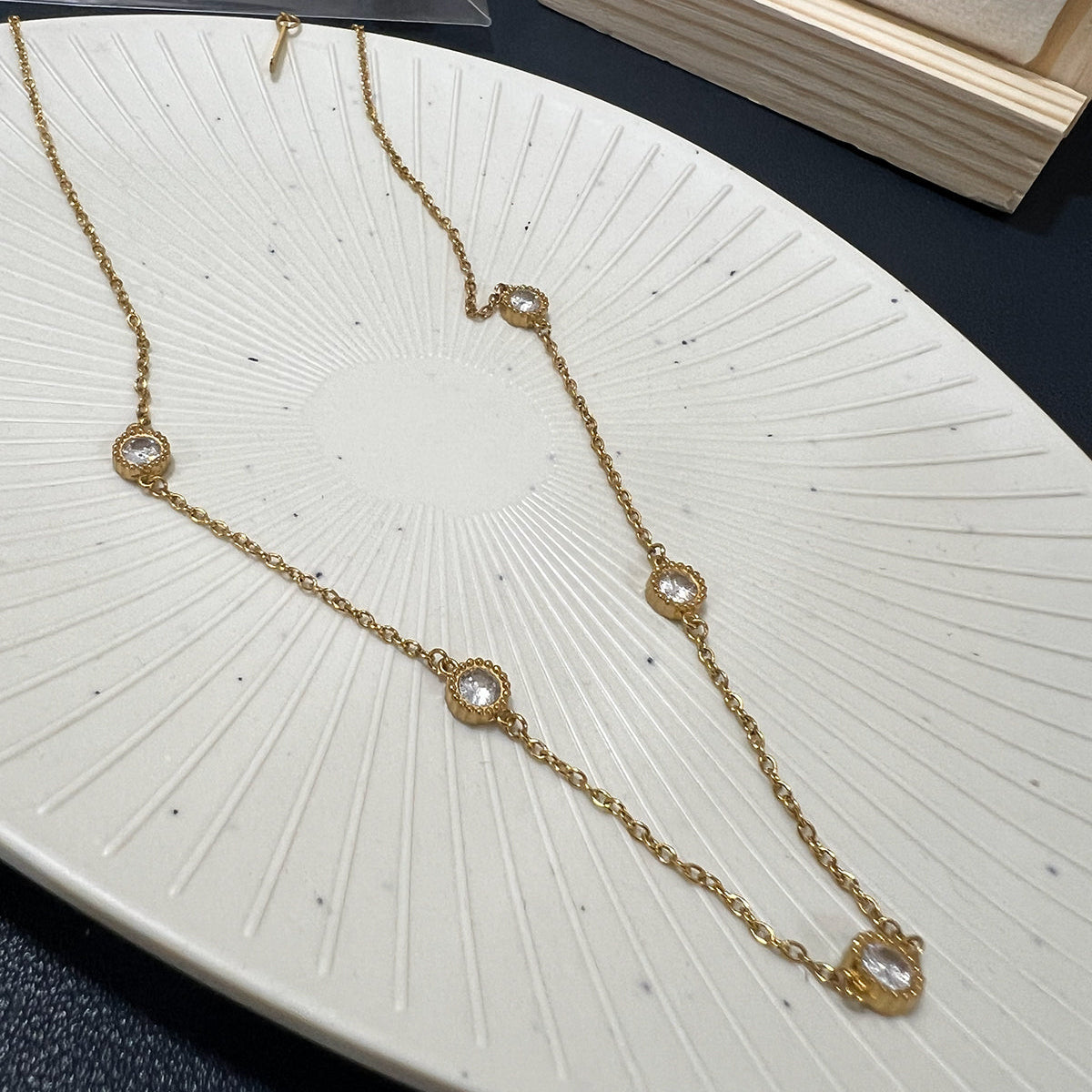 Dainty gold plated necklace featuring circular crystal stations laid across a white sunburst textured plate
