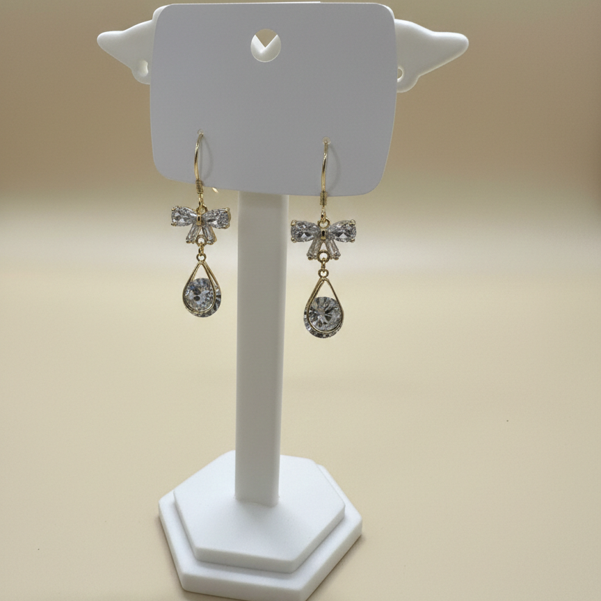 Sparkling gold-plated bow earrings with a crystal teardrop drop displayed on a professional white stand