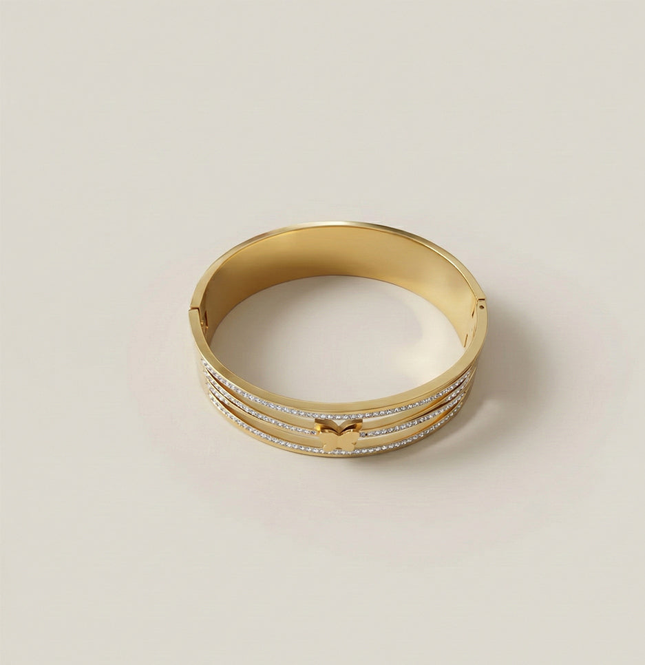 Top view of a gold plated multi-layer bangle featuring a crystal butterfly motif on a neutral background