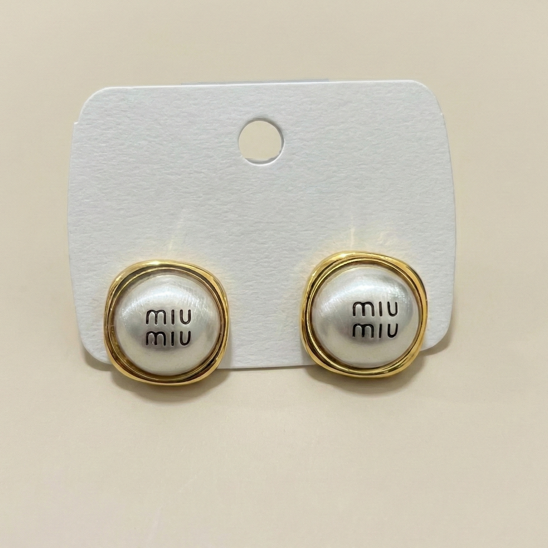 Front view of gold plated monogram button earrings with an anti-tarnish stainless steel finish on a display card