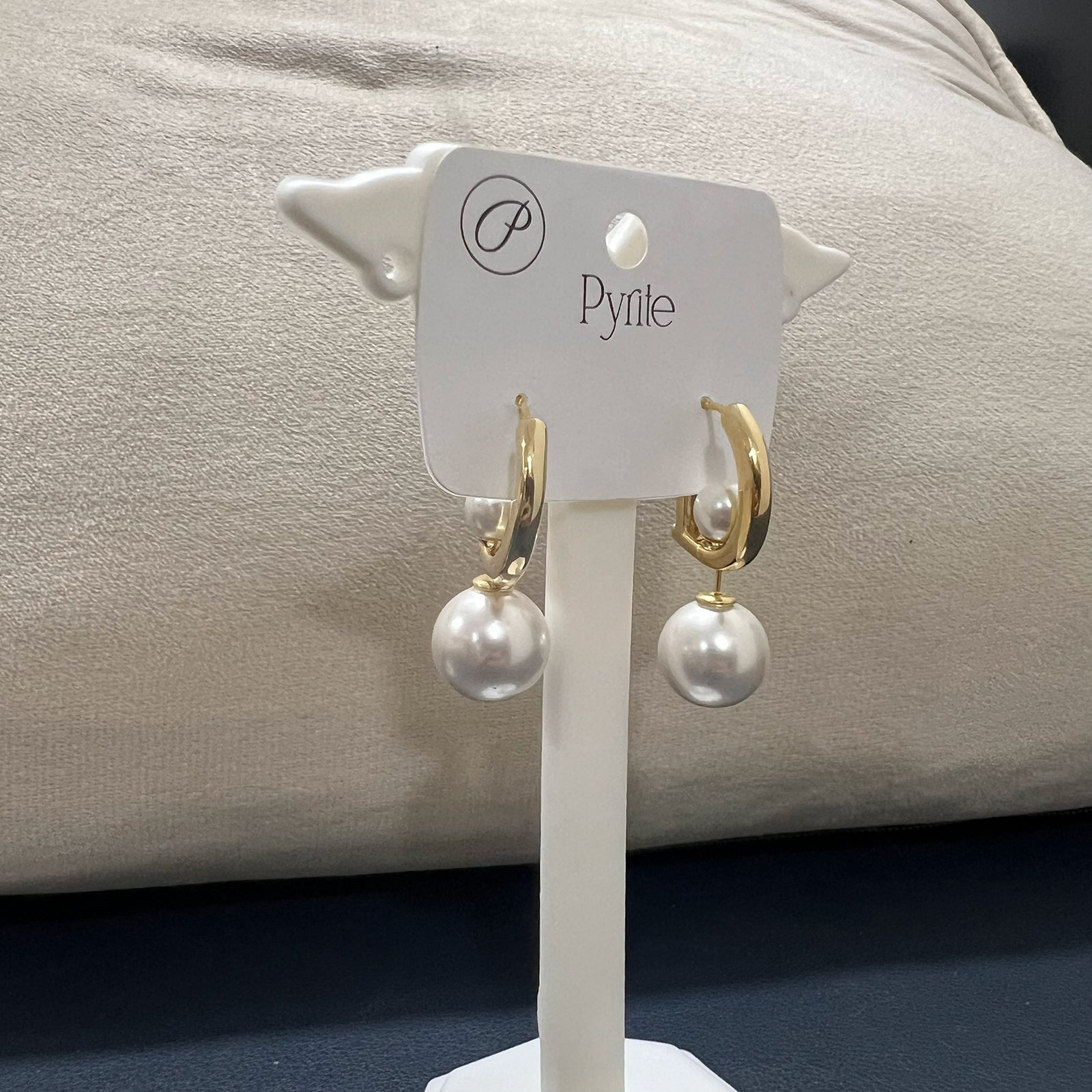 Side profile of a D letter gold hoop earring with a large white drop pearl displayed on a professional white stand