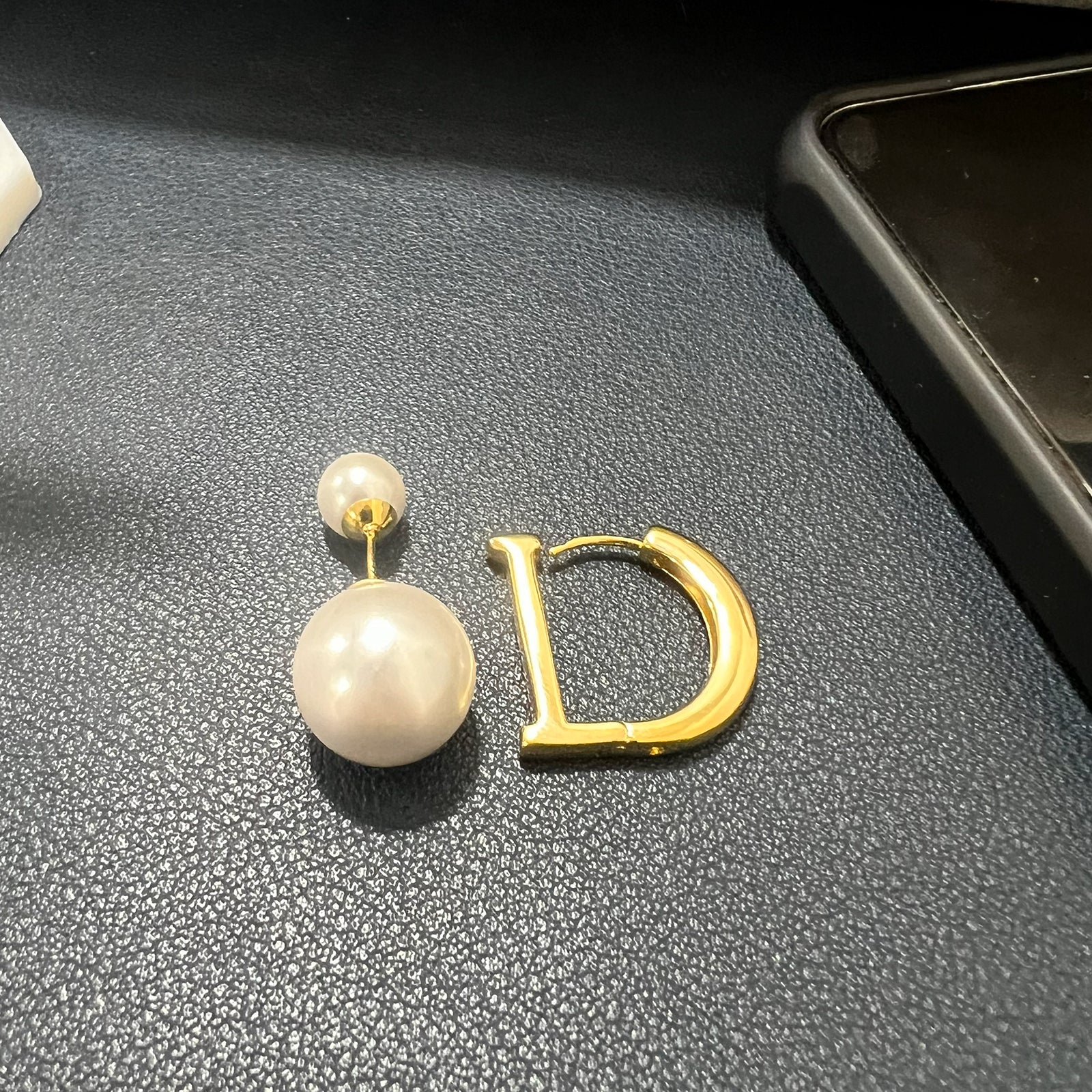Pearl earring with gold 'D' on a textured surface