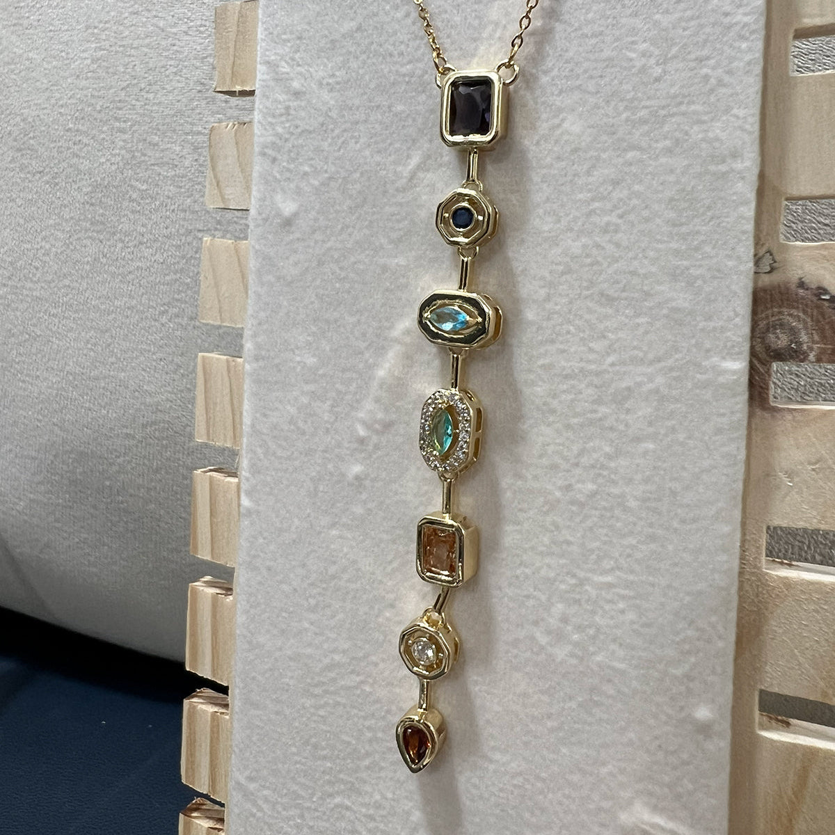 Premium anti-tarnish stainless steel necklace with a linear cascade of colorful gems displayed on a wooden jewelry stand.