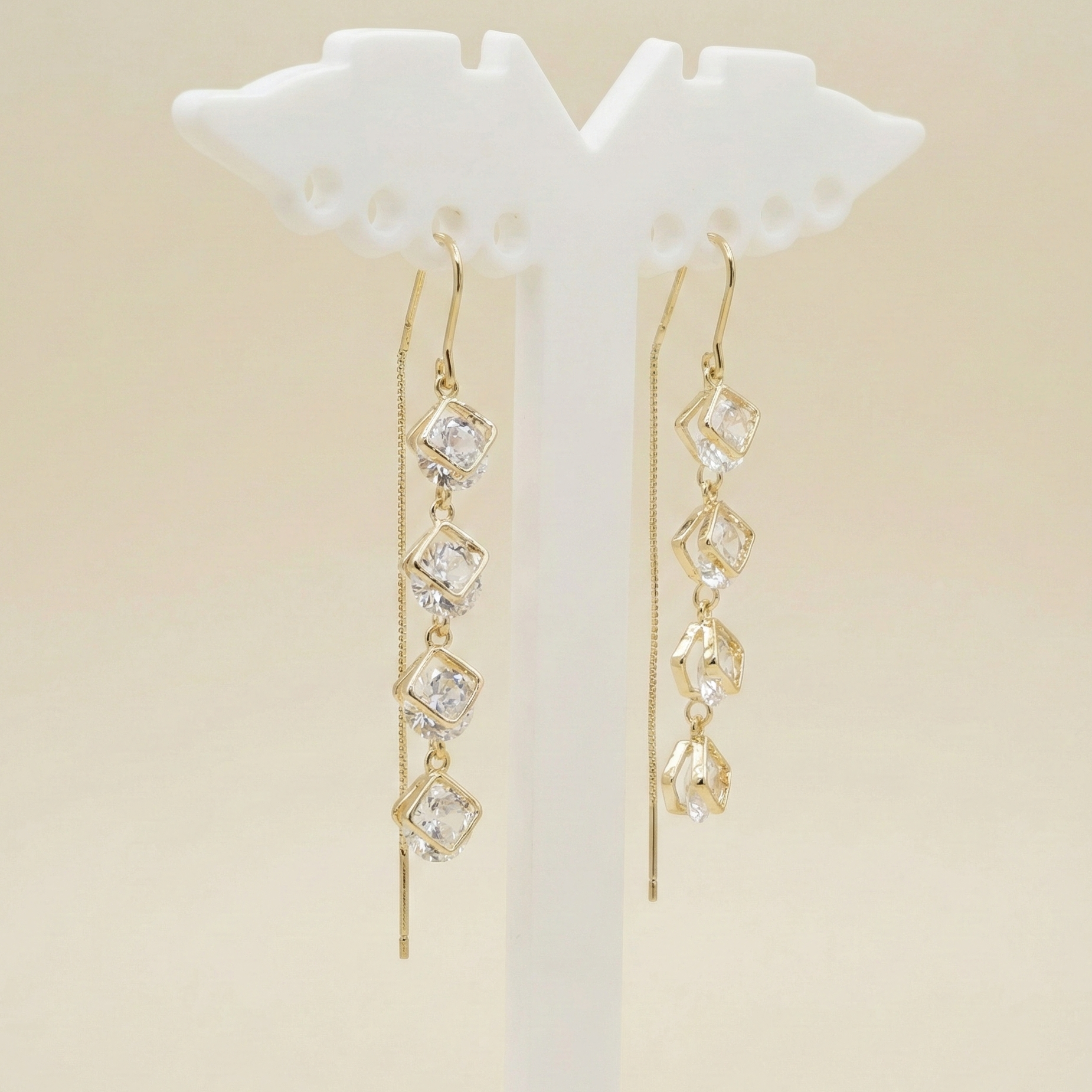 Four-tier square crystal drop earrings with a radiant gold finish displayed on a premium white jewellery stand