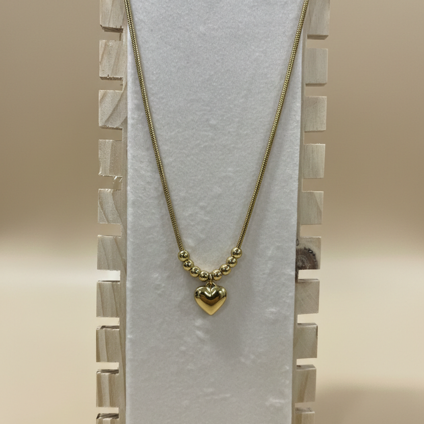A tarnish resistant gold necklace with a polished heart charm displayed vertically on a professional wooden jewelry stand.