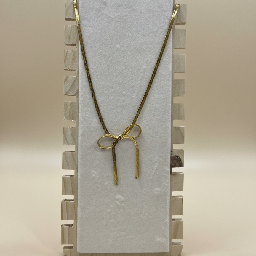 Premium anti-tarnish bow necklace in gold-toned stainless steel draped over a wooden jewelry stand