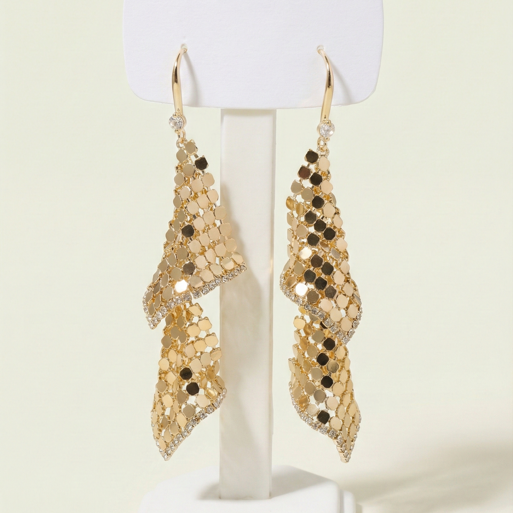Front view of cascading gold plated mesh earrings with crystal trim on a white display stand