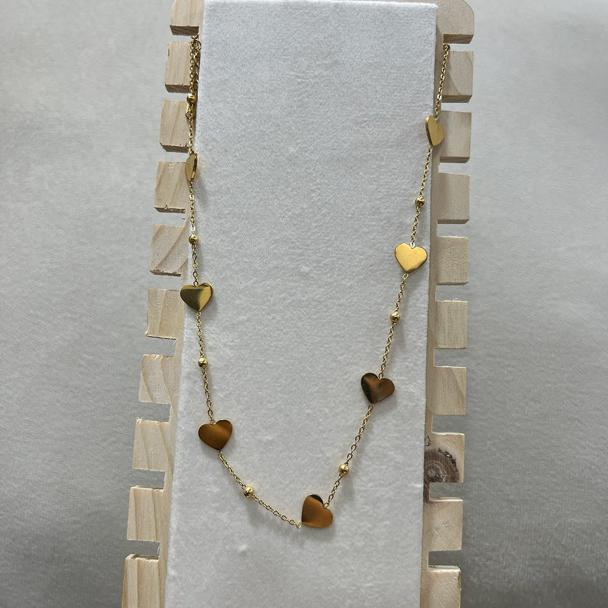 Tarnish resistant heart charm necklace in gold-toned stainless steel displayed on a professional jewelry stand.