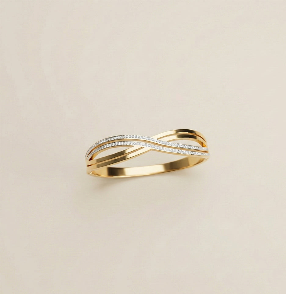 Top view of a gold plated criss cross bangle with stone embellishments on a neutral background