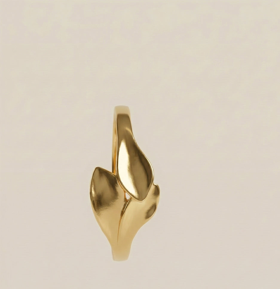 Top view of a polished gold plated leaf motif anti-tarnish bracelet on a neutral cream background