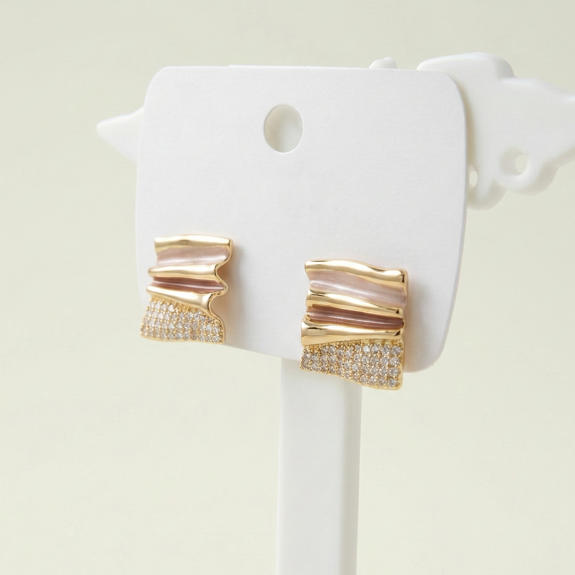 Modern gold plated wave stud earrings with pink accents and crystal pave on a white designer display card