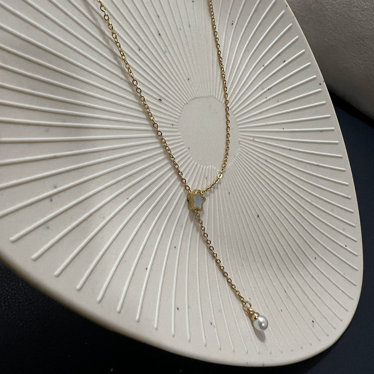 Gold plated lariat necklace featuring a dainty star charm and a white pearl drop on a textured white plate
