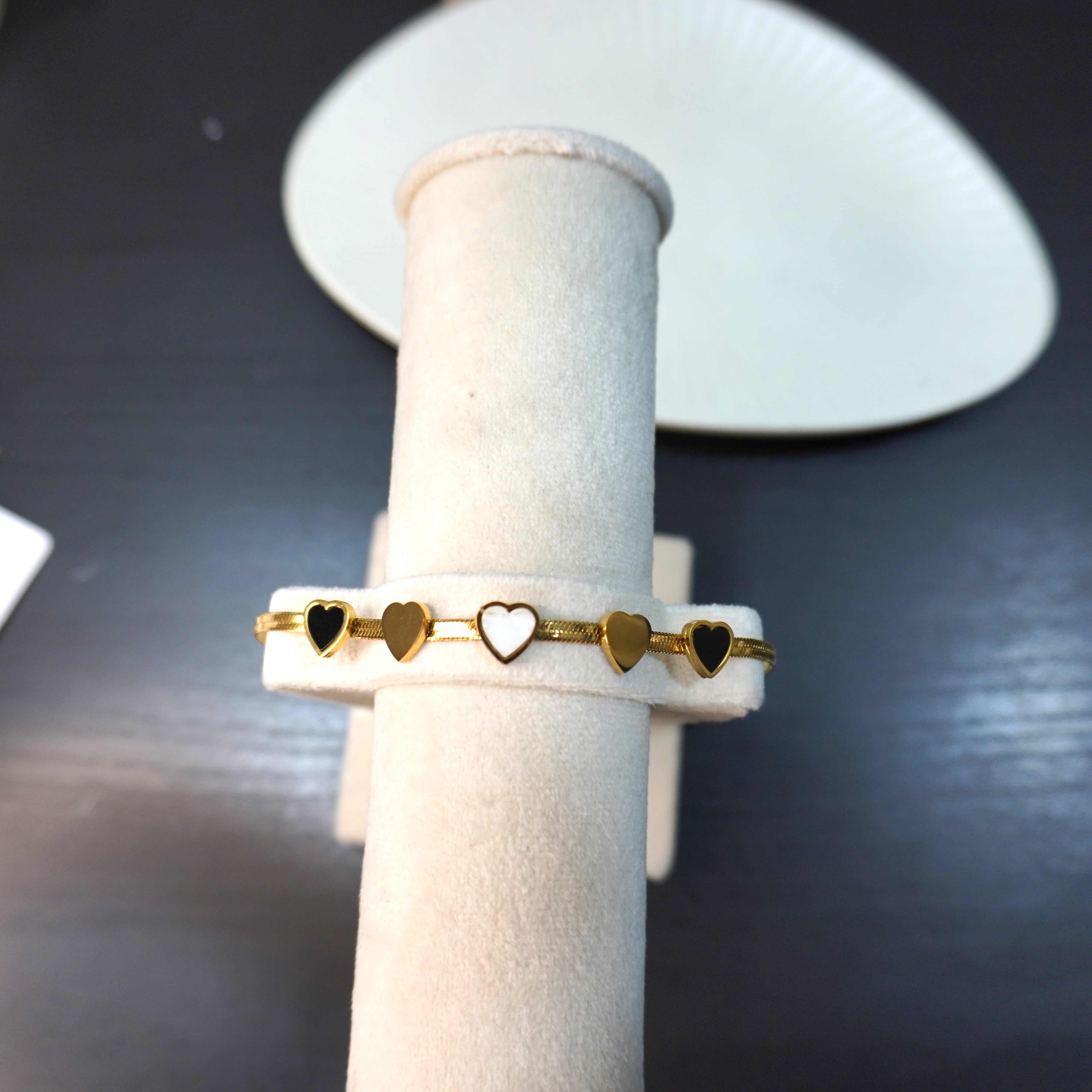 Gold ring with heart-shaped cutouts on a white cylindrical stand against a dark background