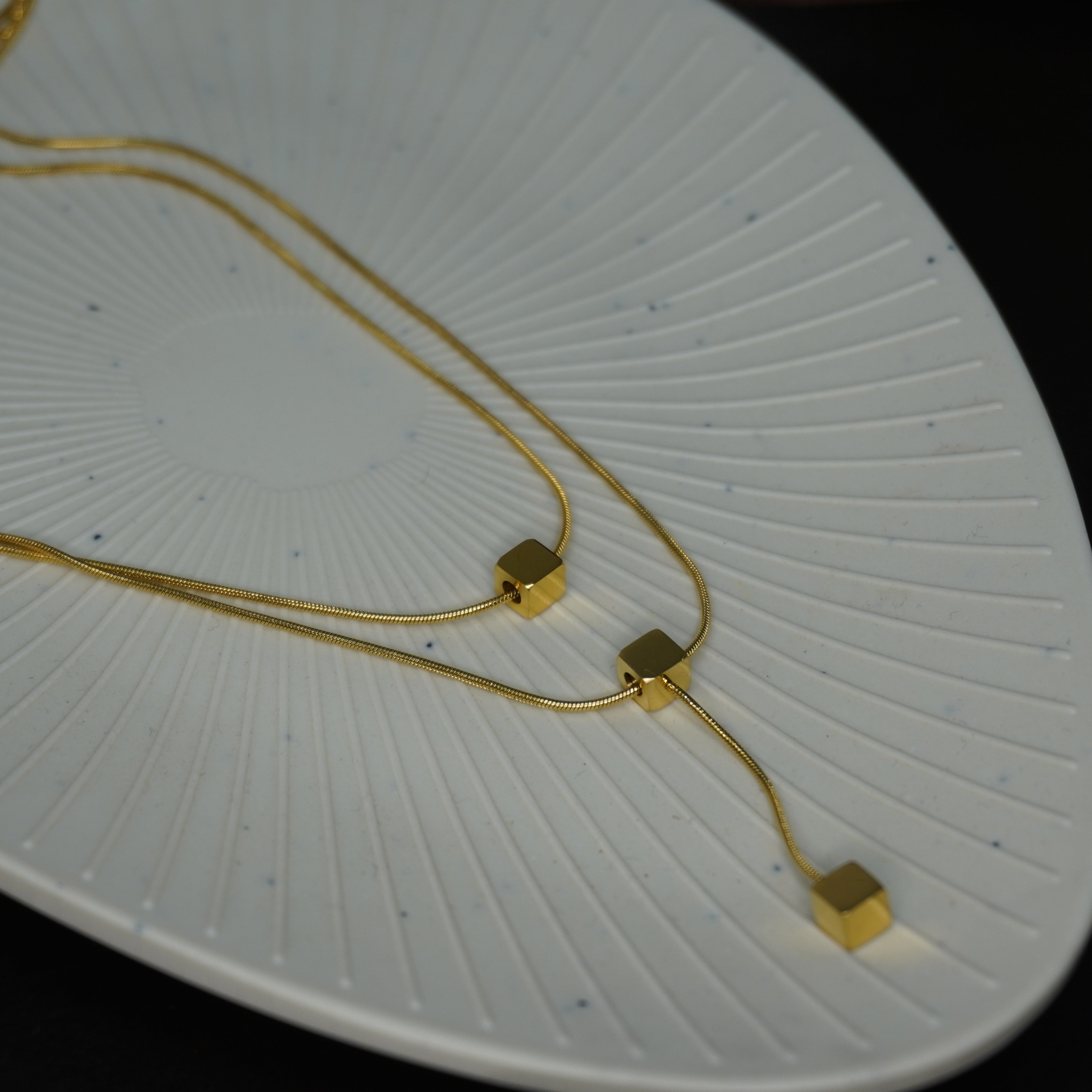 Gold necklace with square pendants on a white textured surface