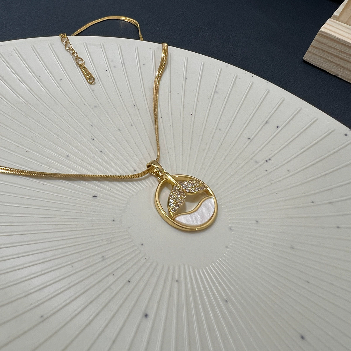 Gold plated whale tail necklace with crystal details resting on a white rippled ceramic tray.