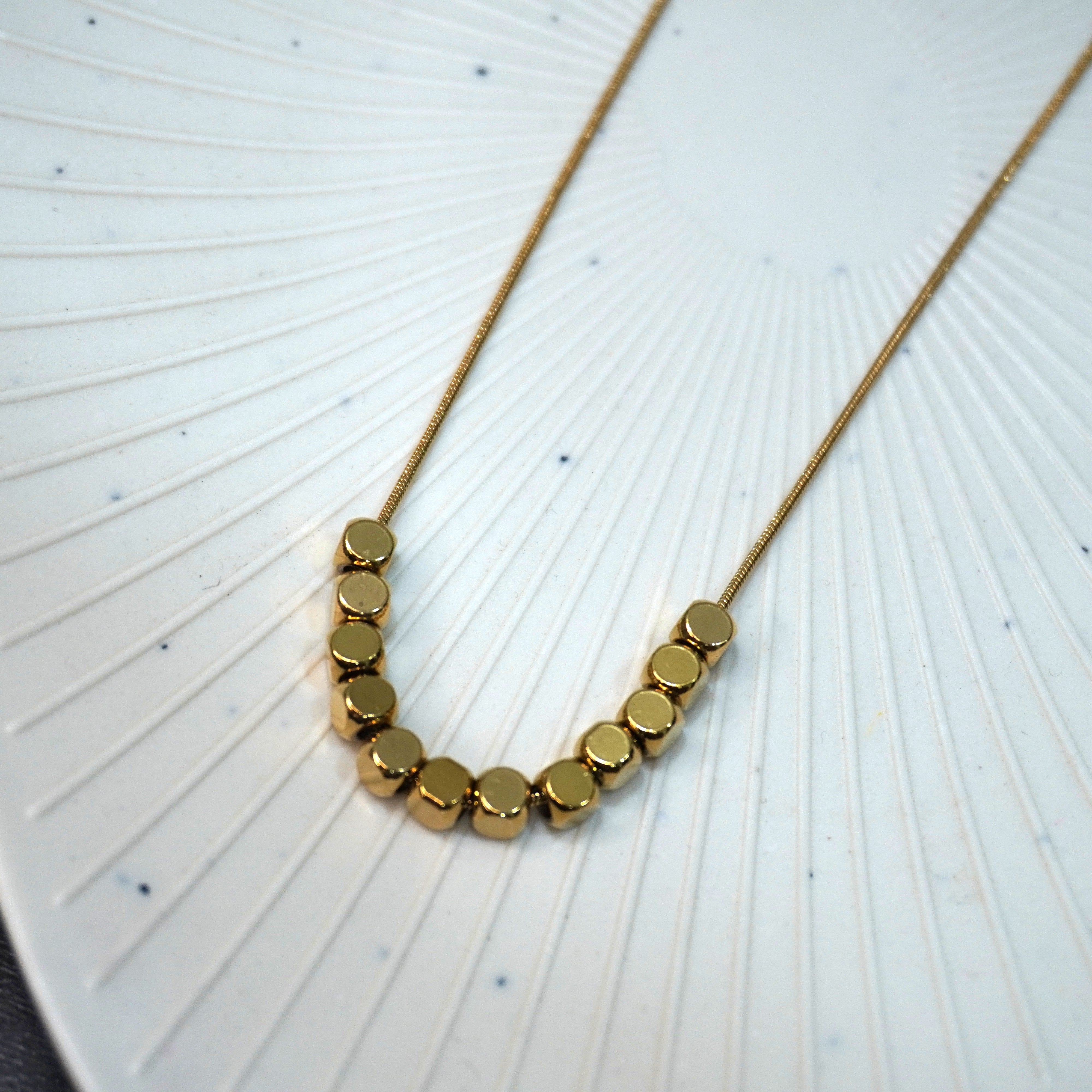 Gold necklace with round beads on a textured white surface