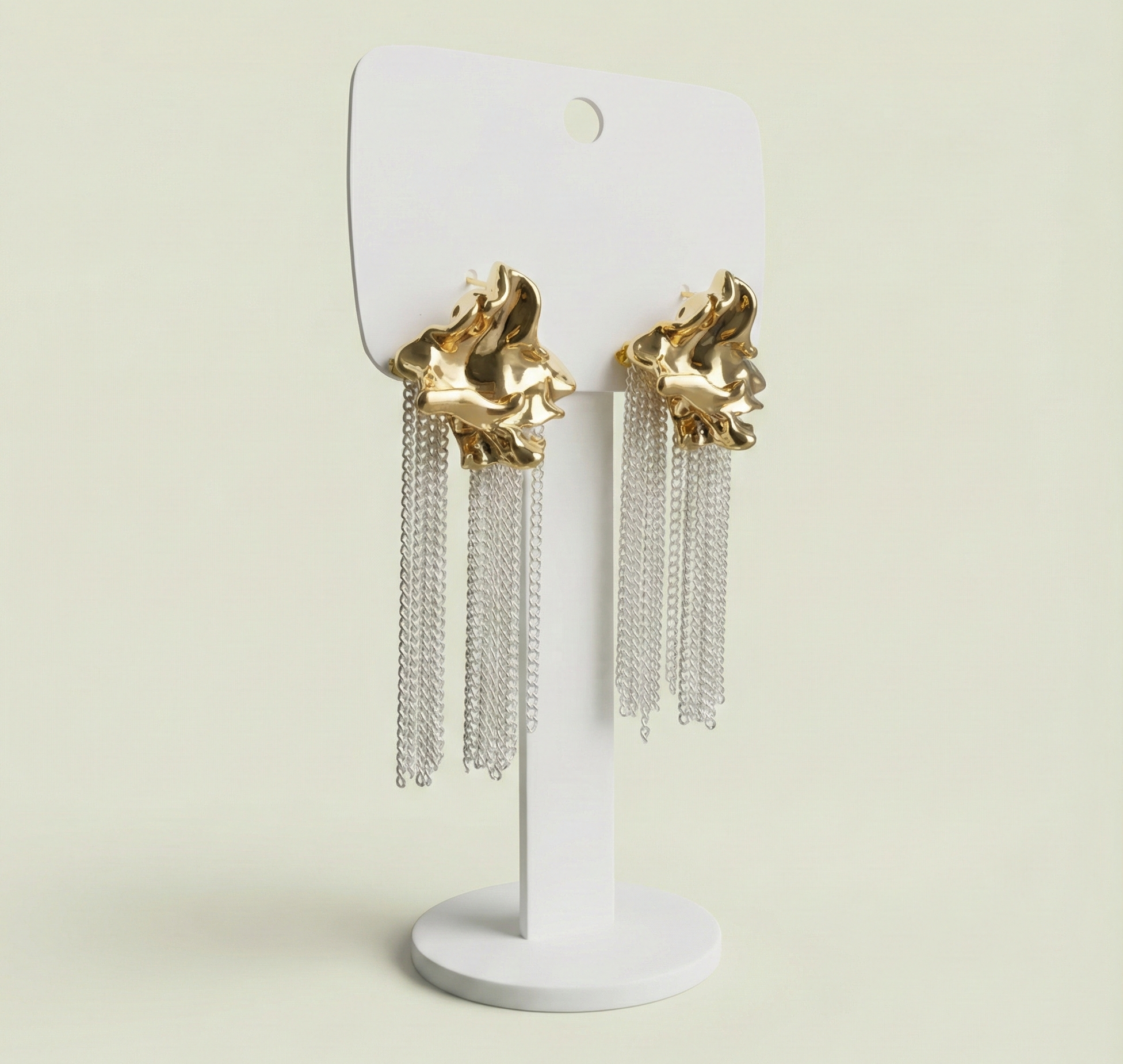 Gold earrings with chain fringes on a white stand against a light beige background