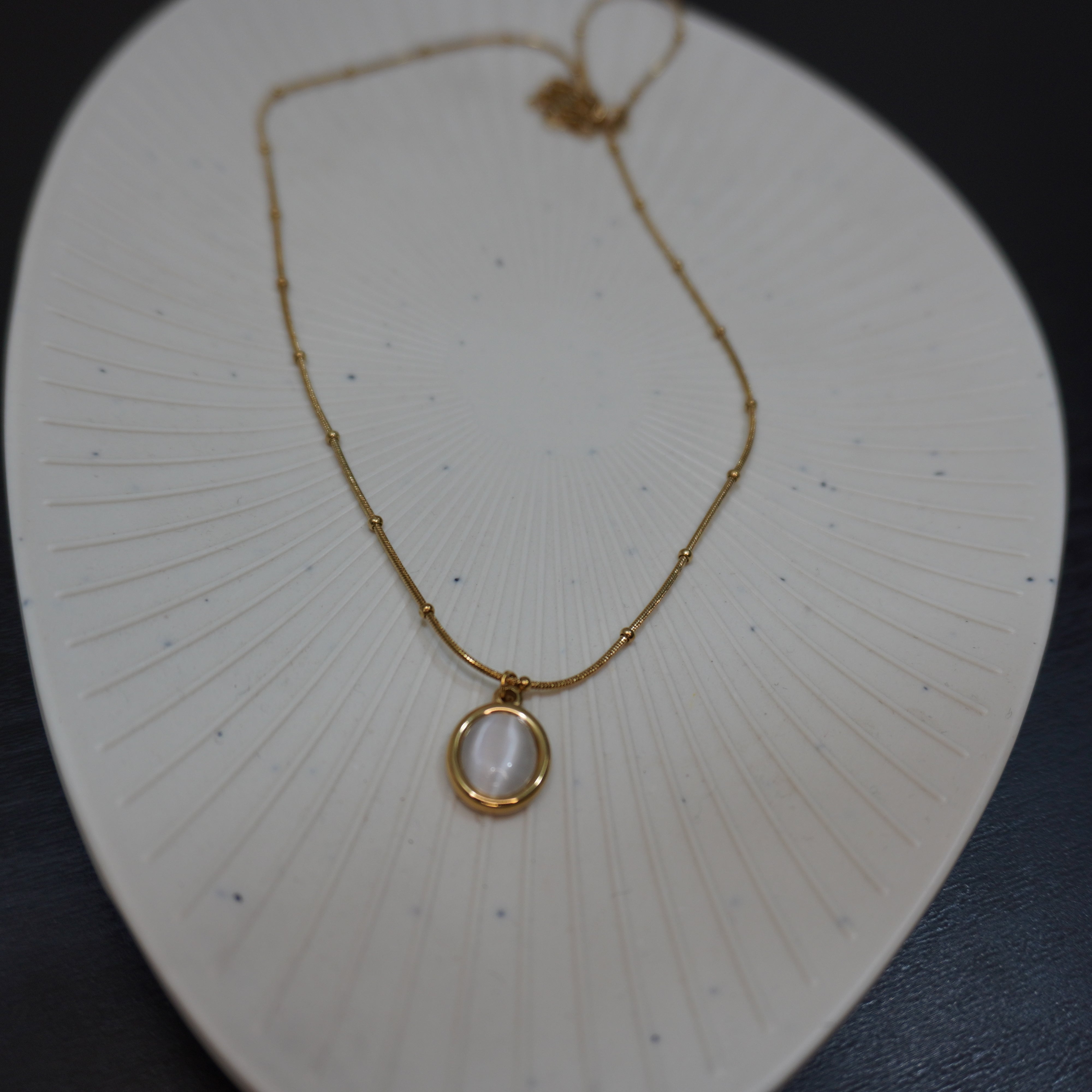 Gold necklace with a pendant on a white textured surface