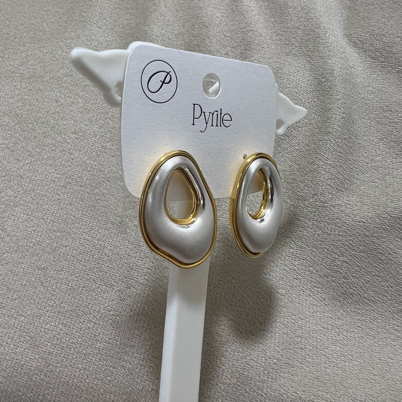 Pair of silver and gold earrings on a card against a gray background