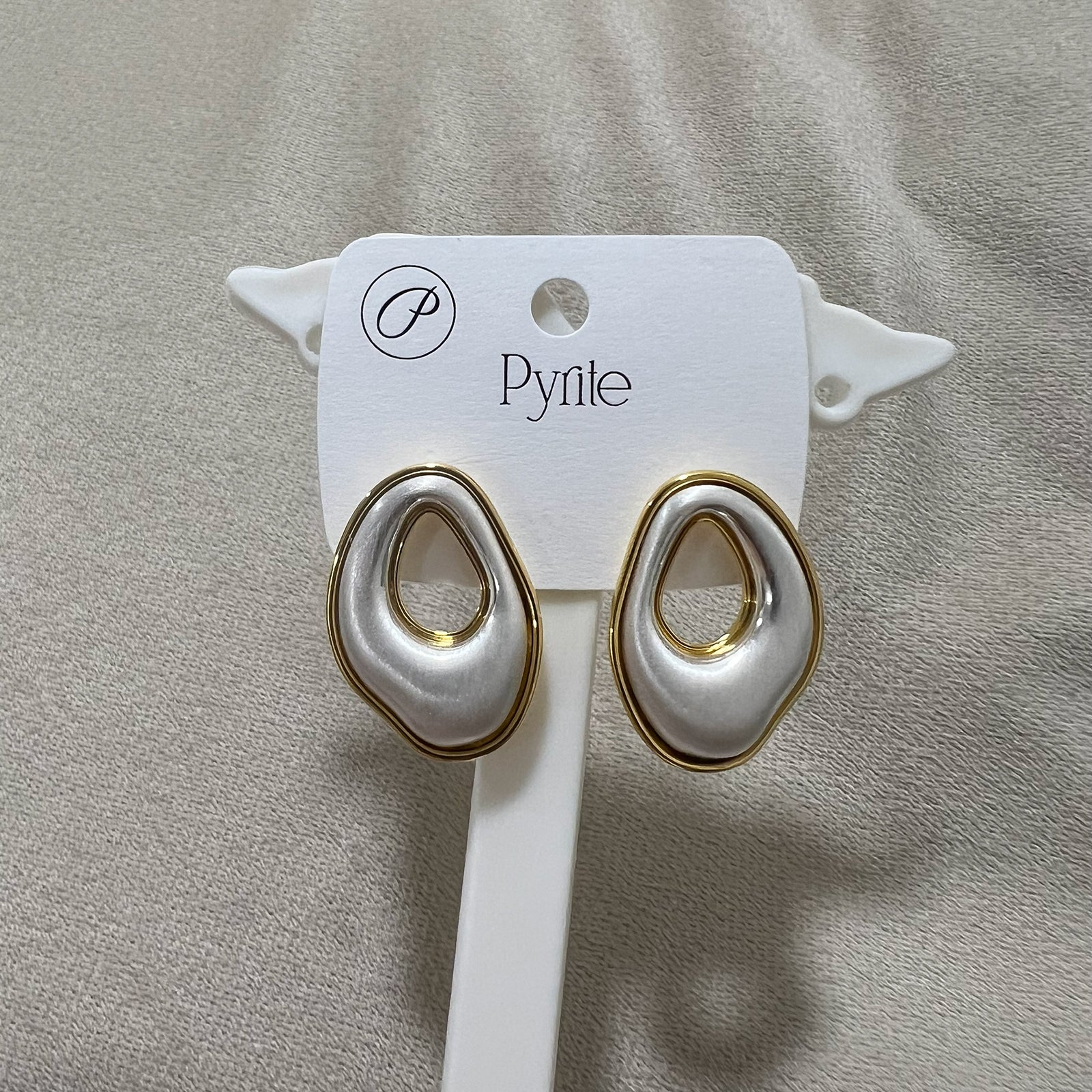 Pair of gold and white earrings on a card against a gray background