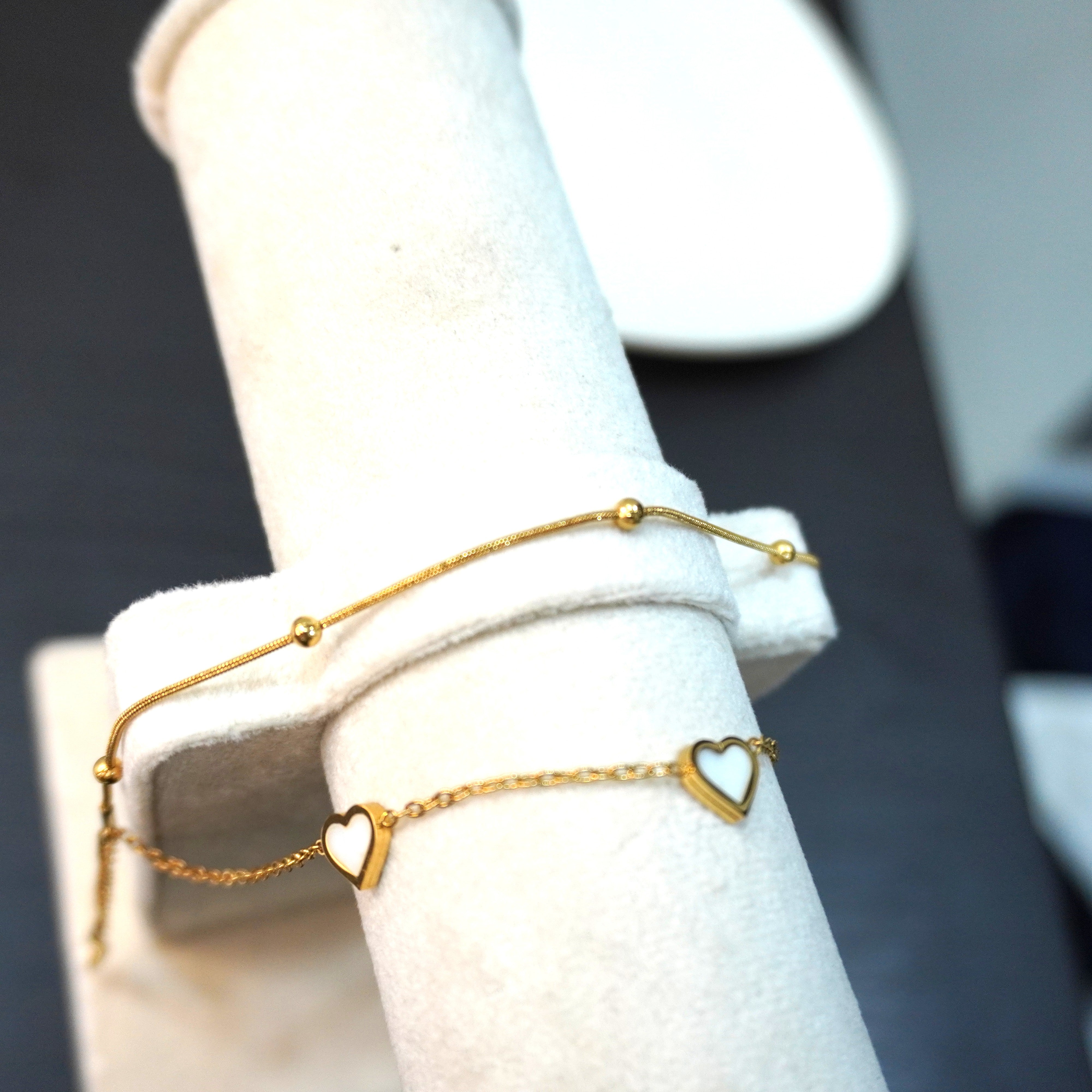 Gold bracelet with heart-shaped charms on a white stand against a dark background
