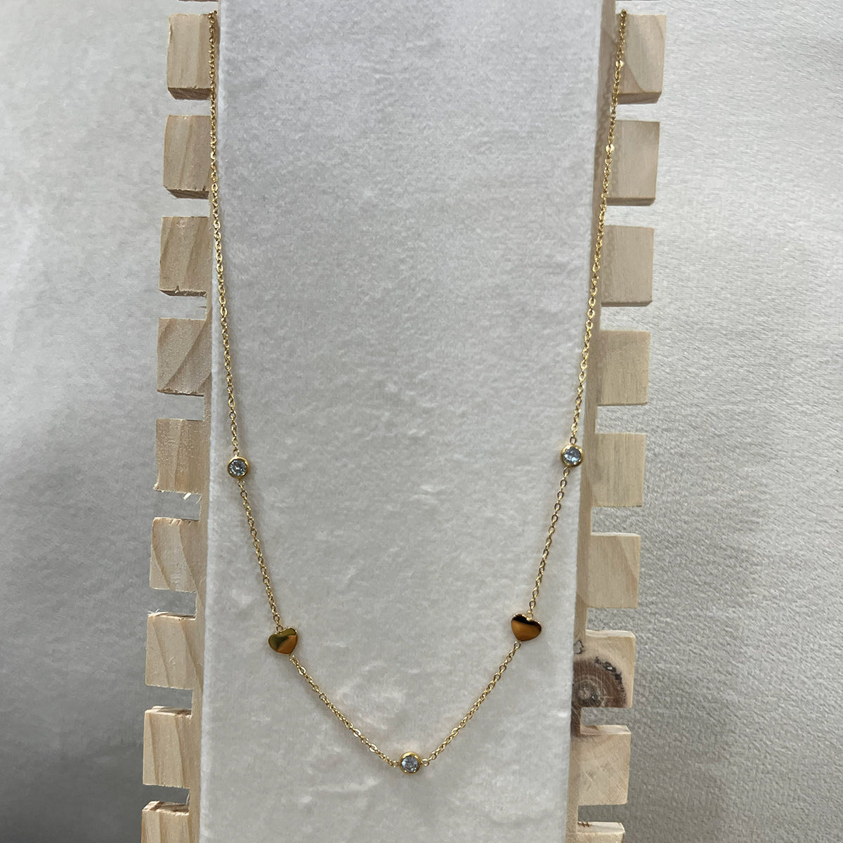 Premium anti-tarnish heart and crystal necklace in gold-toned stainless steel draped over a wooden jewelry stand.