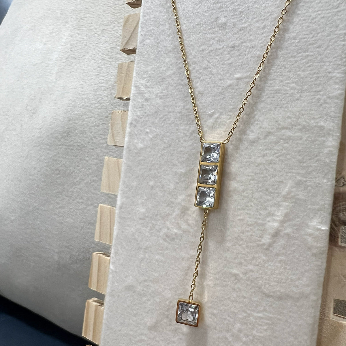 ide profile of a premium anti-tarnish gold finish necklace with a geometric crystal drop on a display stand