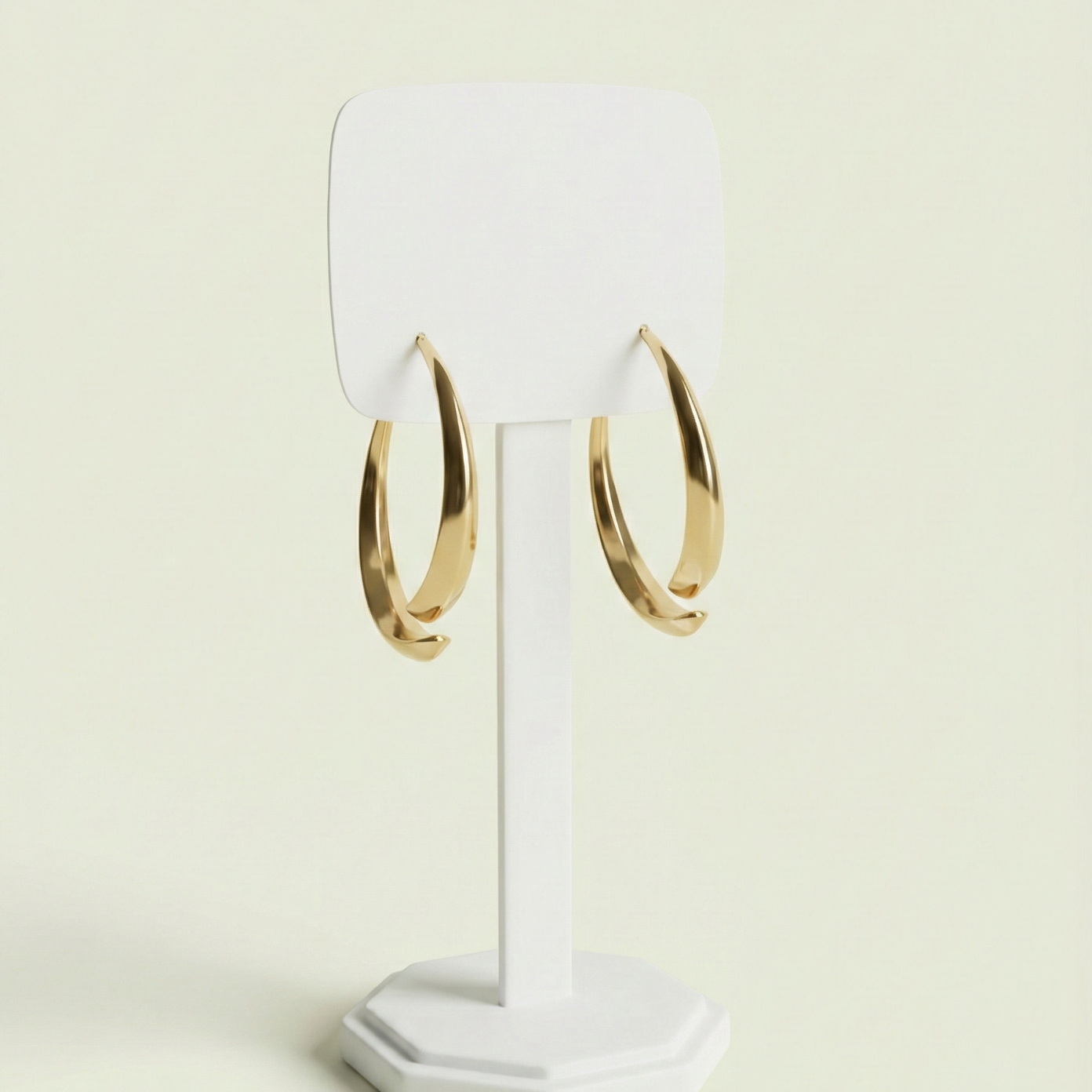 A close-up angled shot of bold, tapered gold-plated hoop earrings on a white jewelry stand - zwelzy design