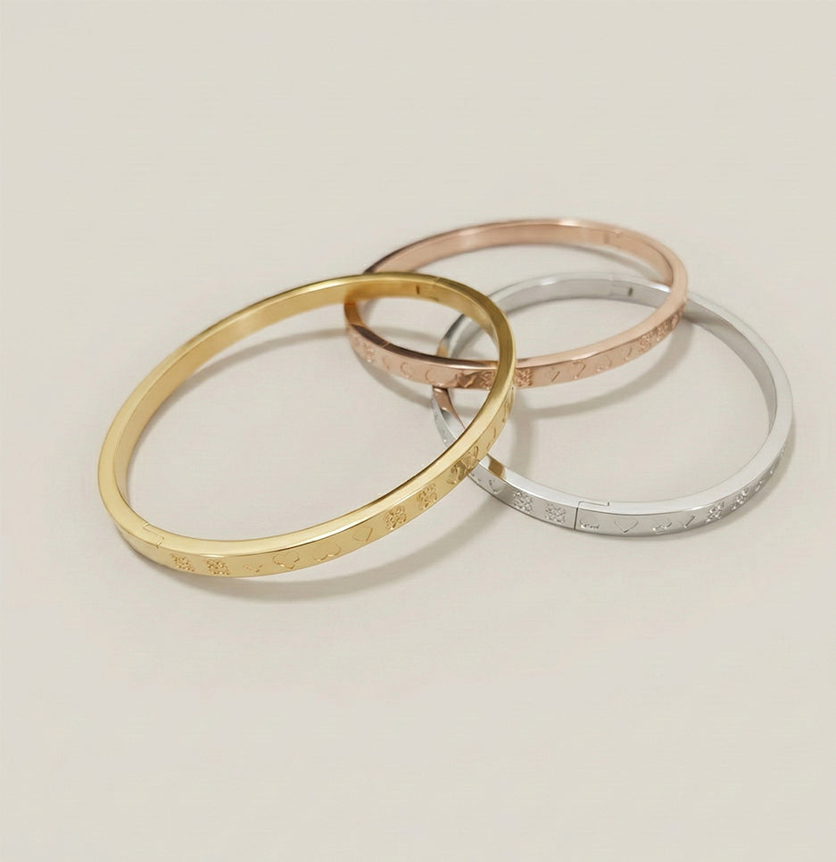A set of three engraved stainless steel bangles in gold, silver, and rose gold finishes on a clean studio background