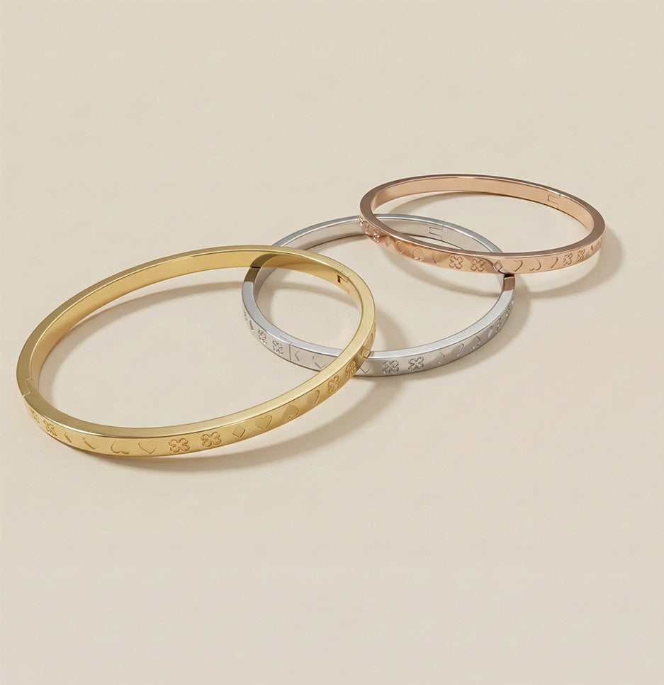 Angled view of three stackable anti-tarnish bracelets featuring delicate heart and clover engravings for daily wear.