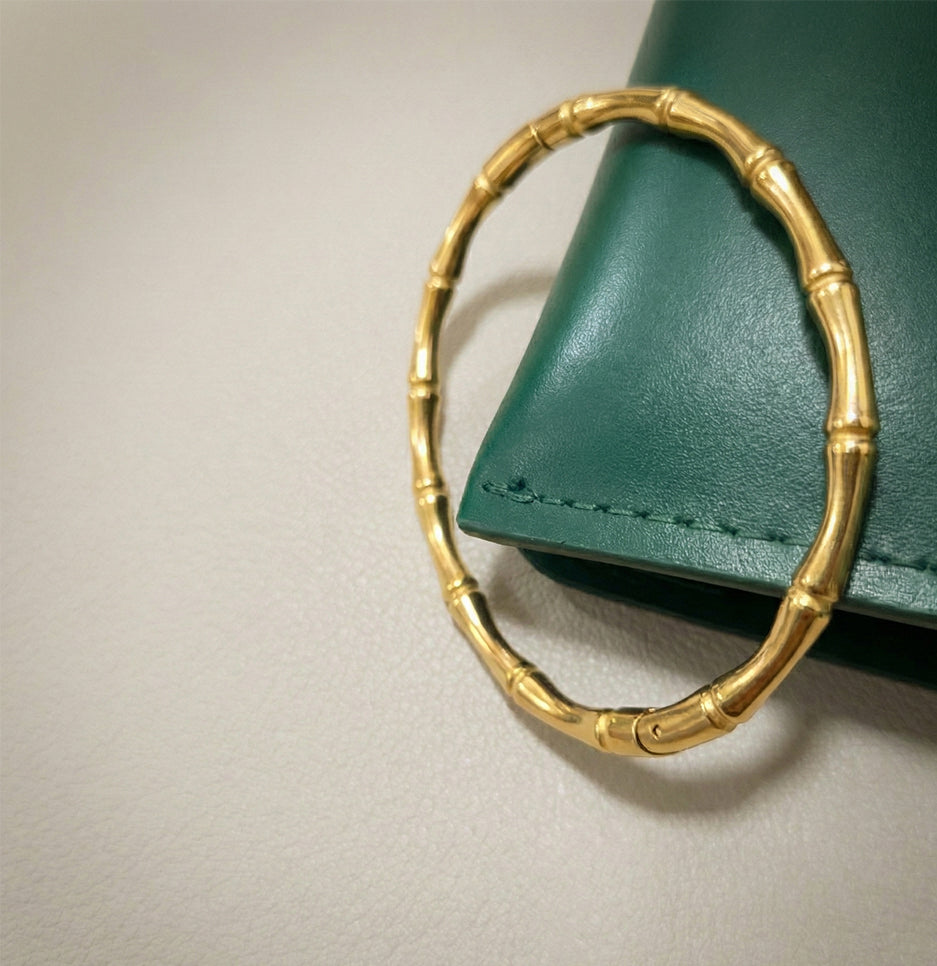 Close up of a stainless steel anti-tarnish bamboo bracelet leaning against a forest green leather accessory