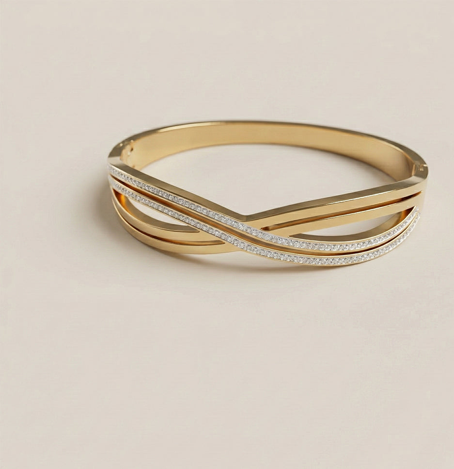 Top view of a gold plated criss cross bangle with stone embellishments on a neutral background