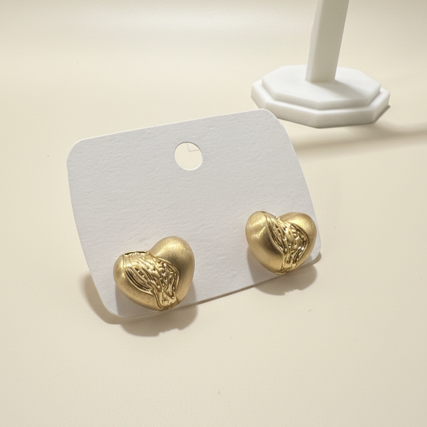 Top down view of textured gold plated heart stud earrings on a white display card featuring a rippled metallic design