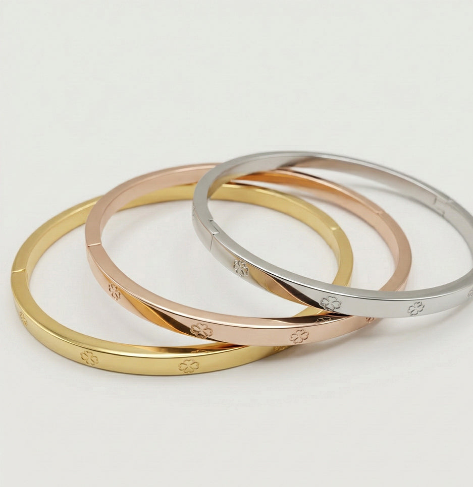 Angled view of three stackable anti-tarnish clover motif bracelets made from premium gold-plated stainless steel