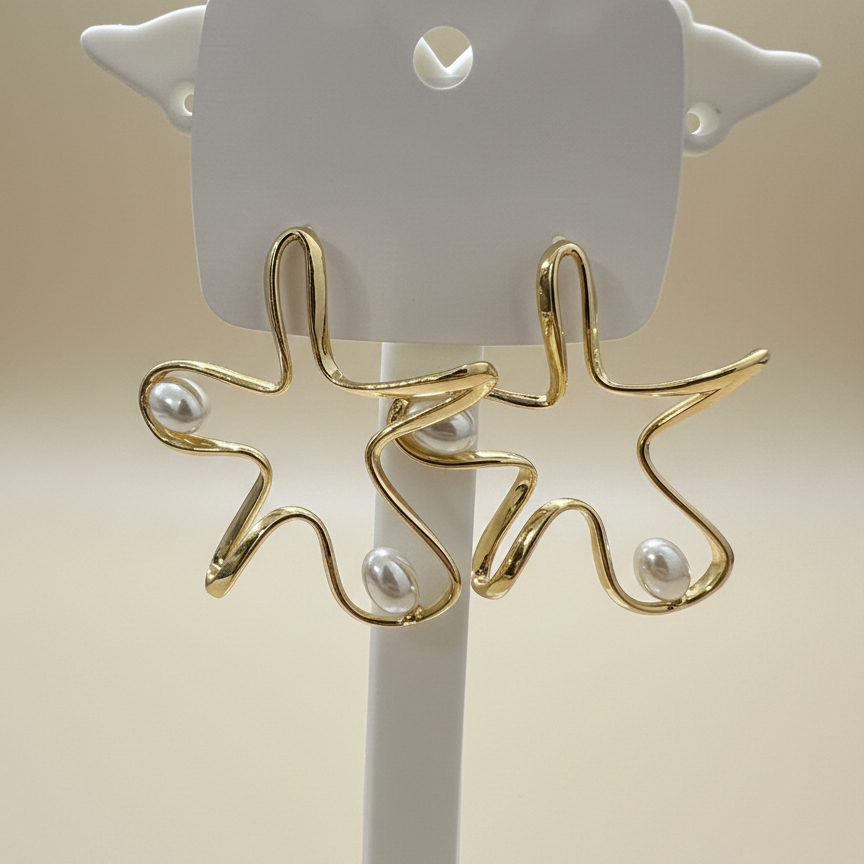 Gold plated abstract wavy star earrings with three pearls displayed on a white jewelry stand.