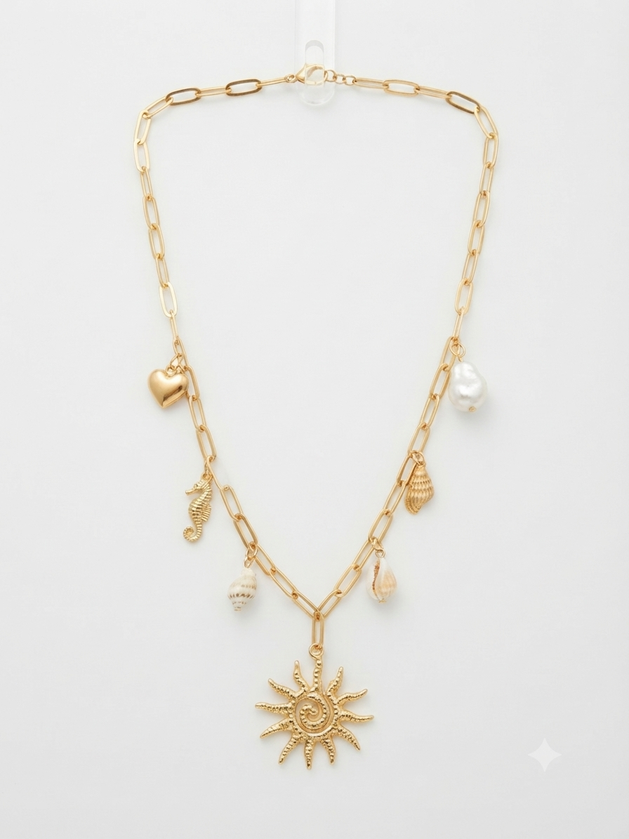 A gold-tone layered necklace featuring paperclip chain, a sun pendant, and small charms including a heart, seahorse, shells, and a pearl-like bead, displayed on a light gray background.