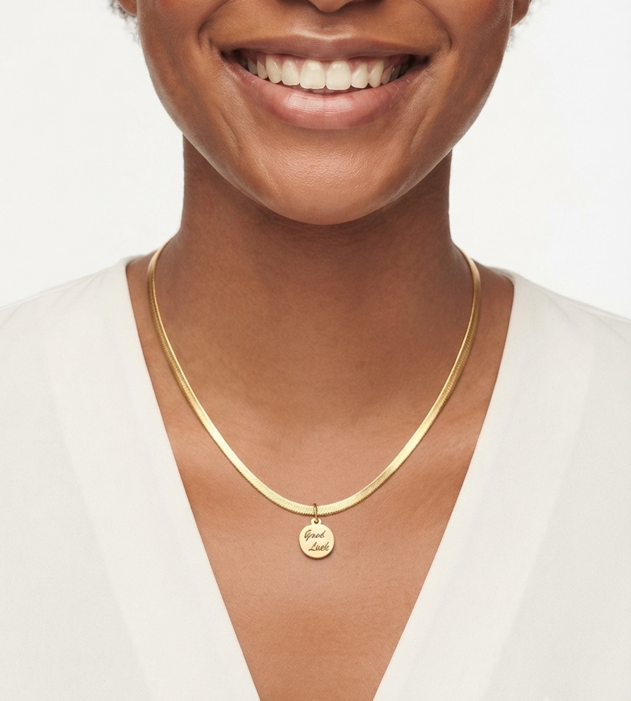 Gold-tone herringbone necklace with round Good Luck pendant worn on a woman, elegant minimalist jewelry